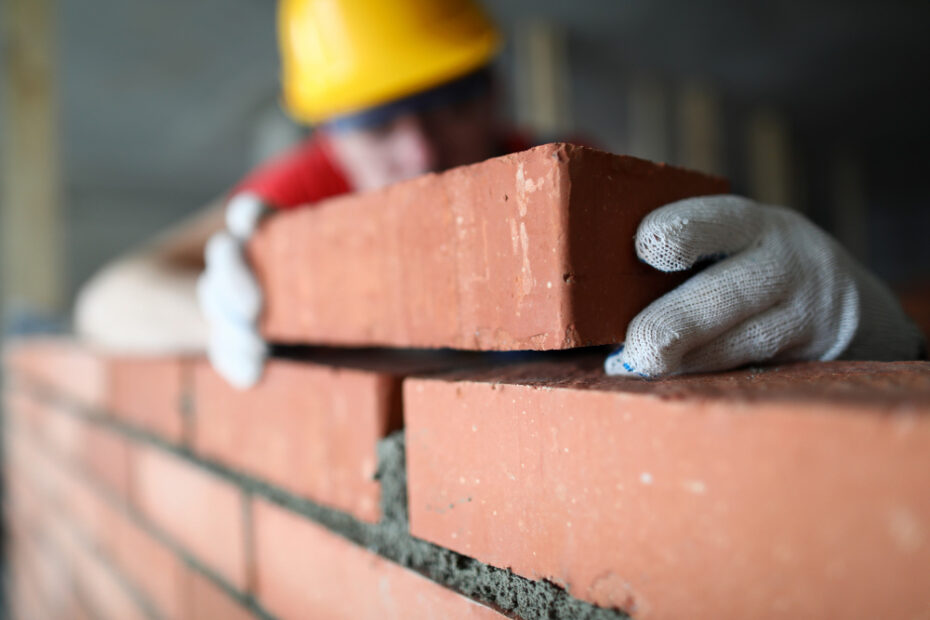 close up professional construction worker laying bricks industrial site builder protective uniform man building wall with blocks renovation concept